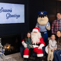 Little girl in green dress on Santa's lap, little boy on mom's lap, and dad behind couch